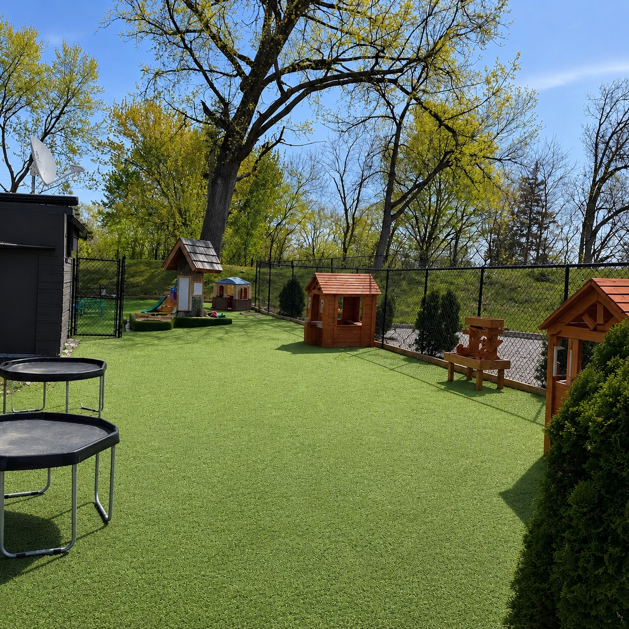 Nature-inspired outdoor play area at Edina Daycare East Campus featuring open green space, wooden playhouses, climbing activities, and opportunities for active outdoor exploration.