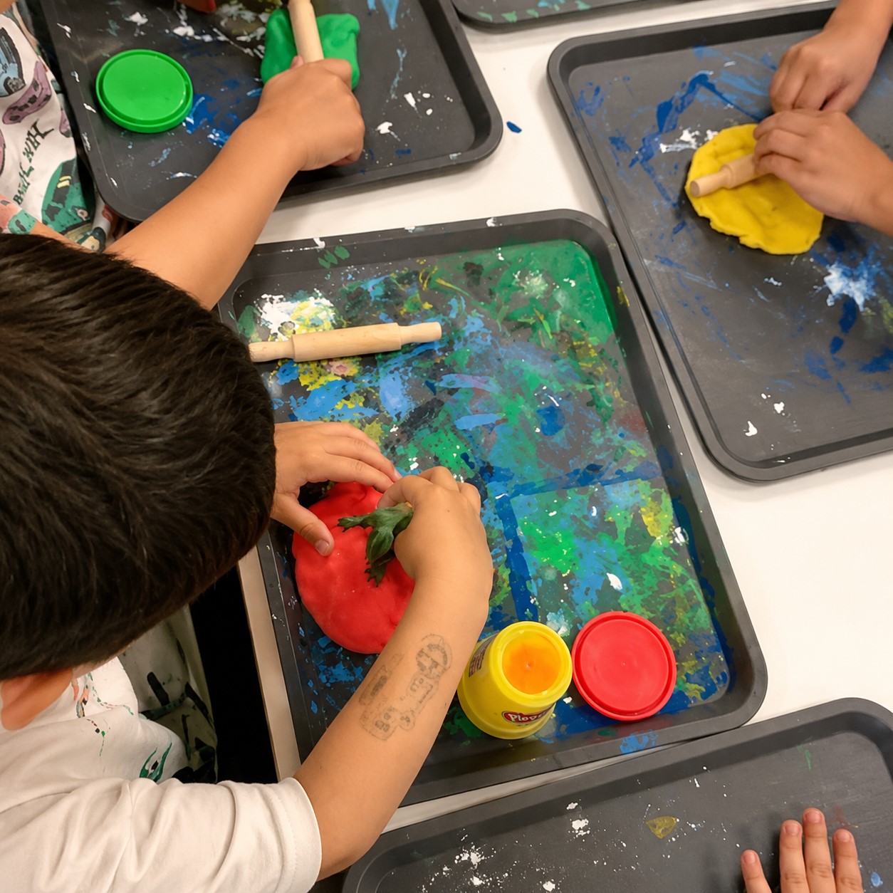 Children explore creativity and sensory learning through hands-on play with colorful dough and rolling tools at Edina Daycare.