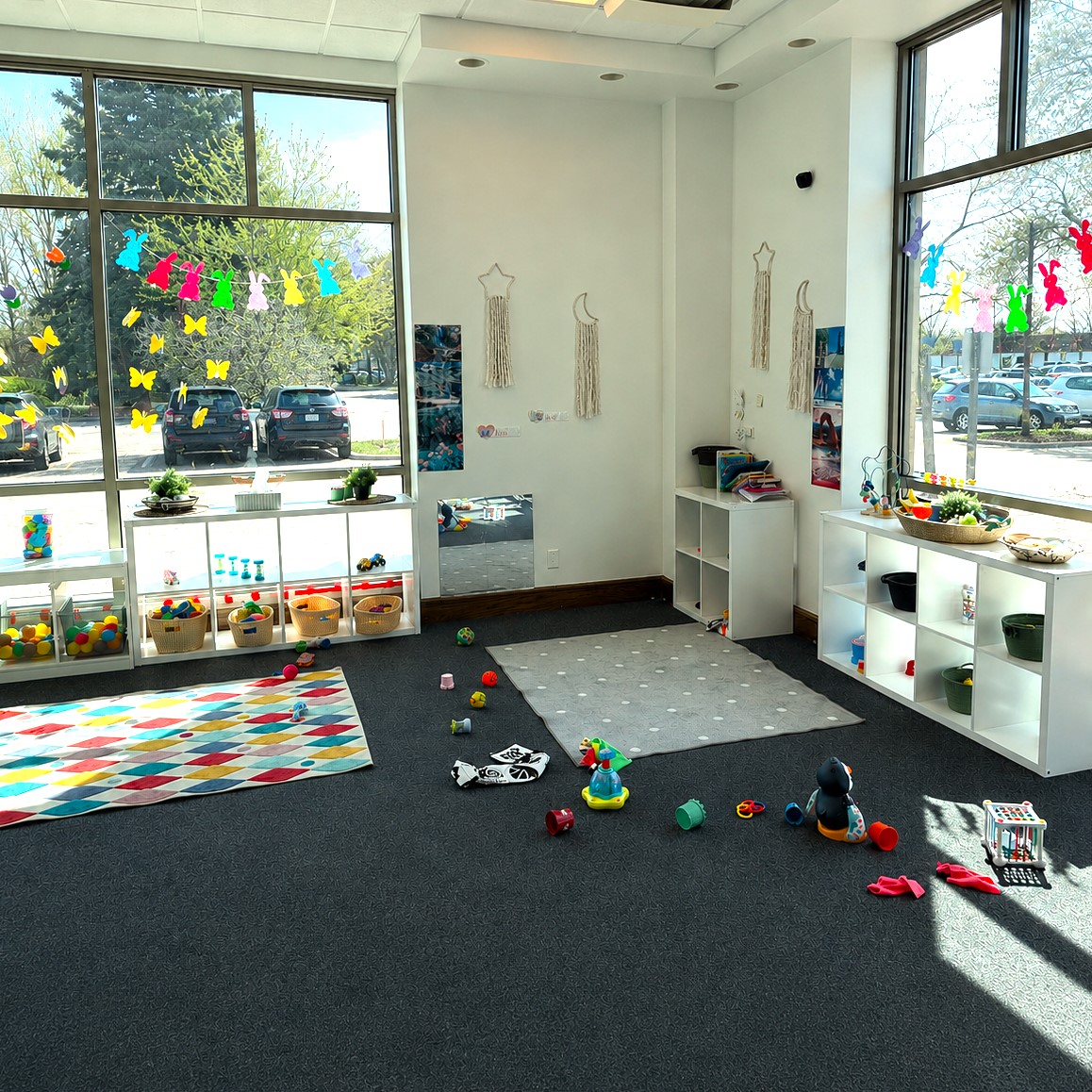 Bright, organized infant classroom with natural light, low open shelves of toys, and soft play areas, designed to support independent exploration, early learning, and responsive caregiving routines at Edina Daycare.