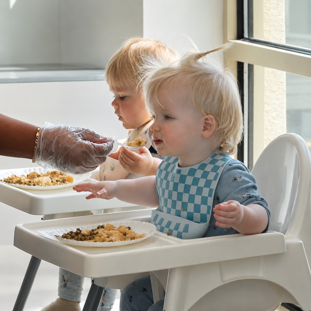 Infants seated in highchairs receiving attentive, one-on-one feeding from a caregiver, illustrating responsive care and a flexible, child-led feeding schedule in a calm, supportive environment at Edina Daycare.