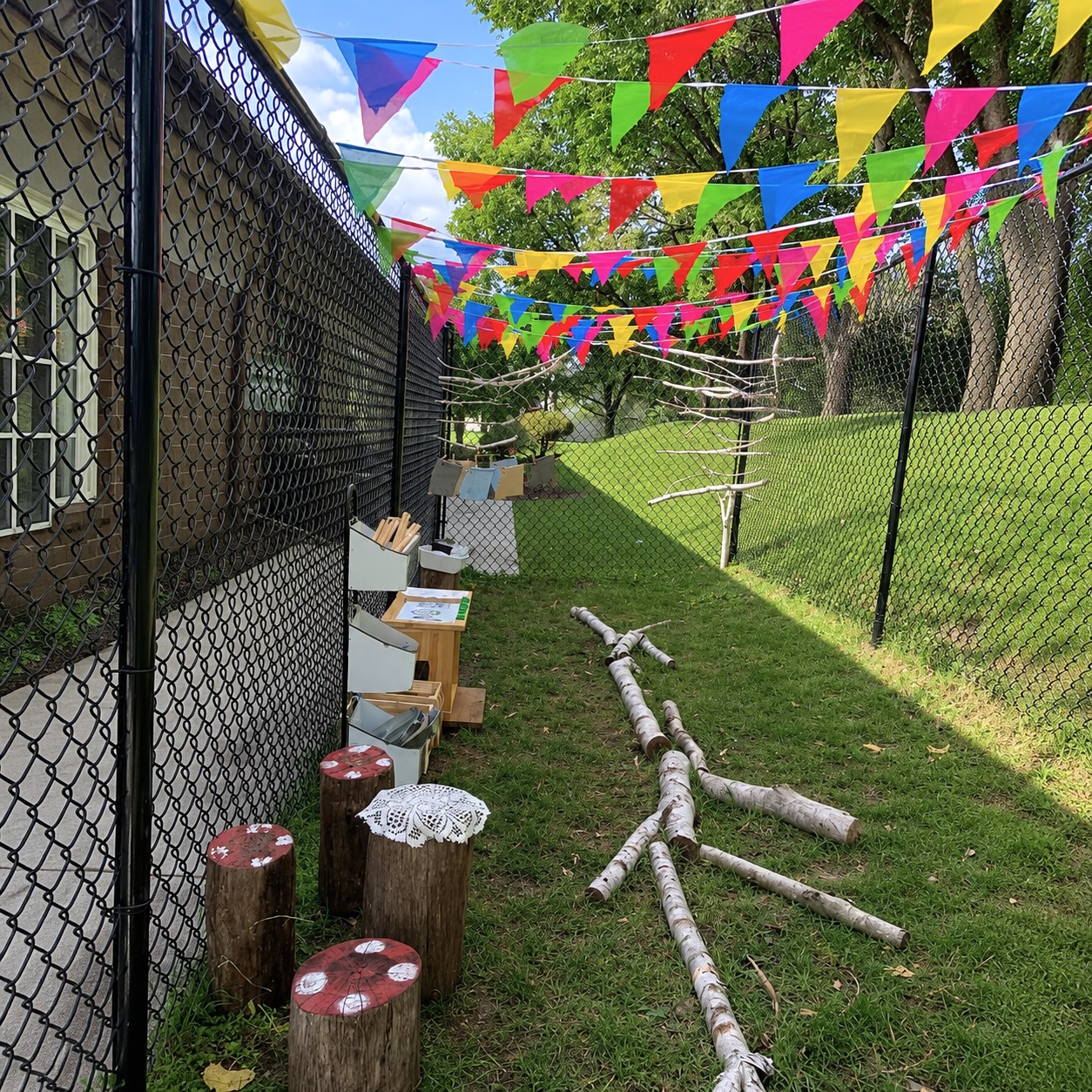 Outdoor learning space with natural materials, logs, and colorful flags at Edina Daycare, encouraging curiosity, exploration, and hands-on discovery through play.