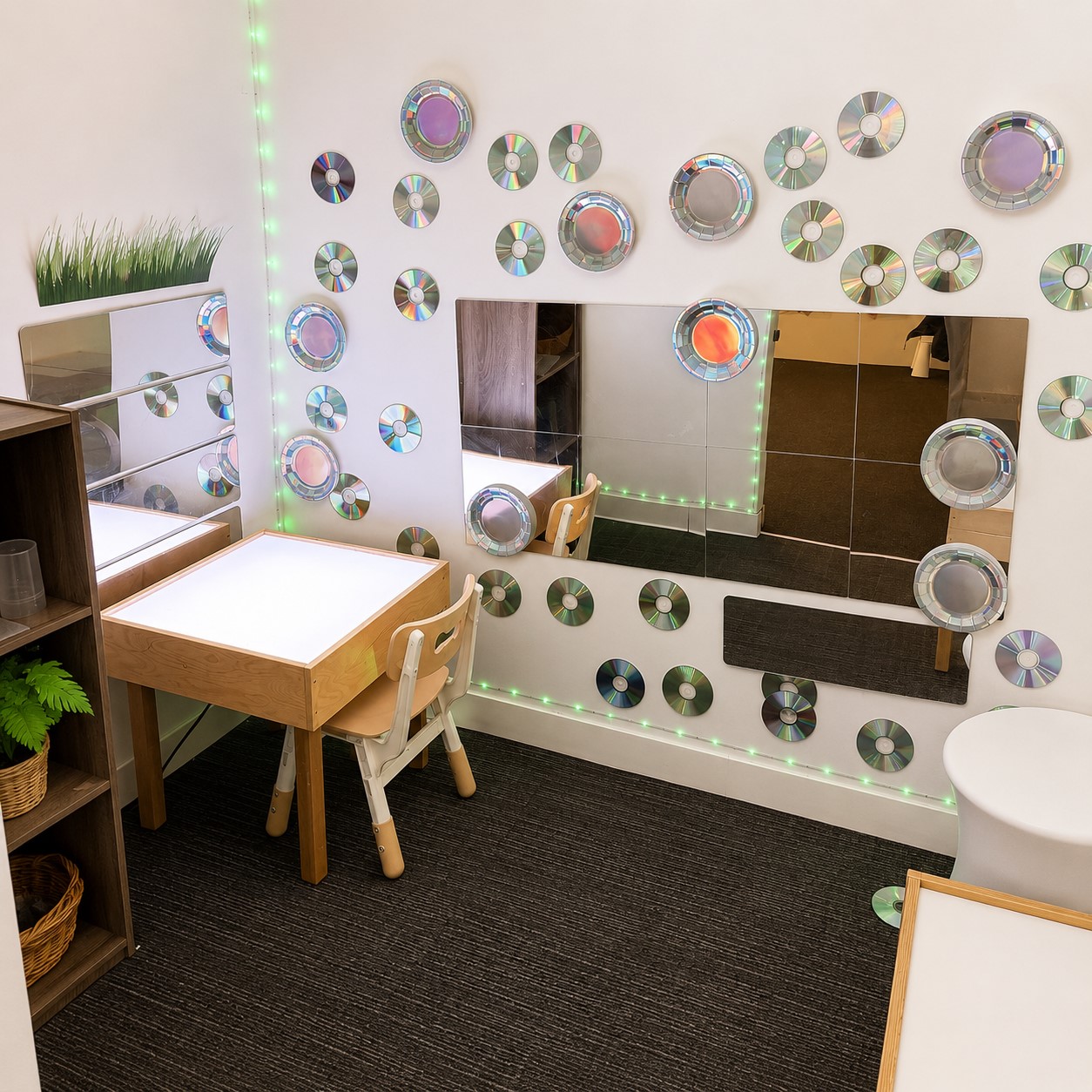 Sensory wall with mirrors, reflective discs, and soft lighting alongside a child-sized table at Edina Daycare, encouraging visual exploration and sensory engagement.